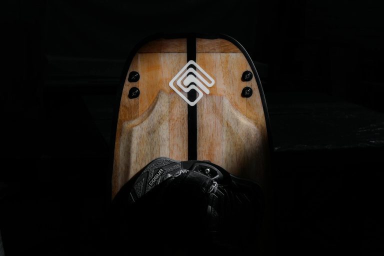 Close-up of a wooden wakeboard featuring a modern logo under spotlight in dark setting.