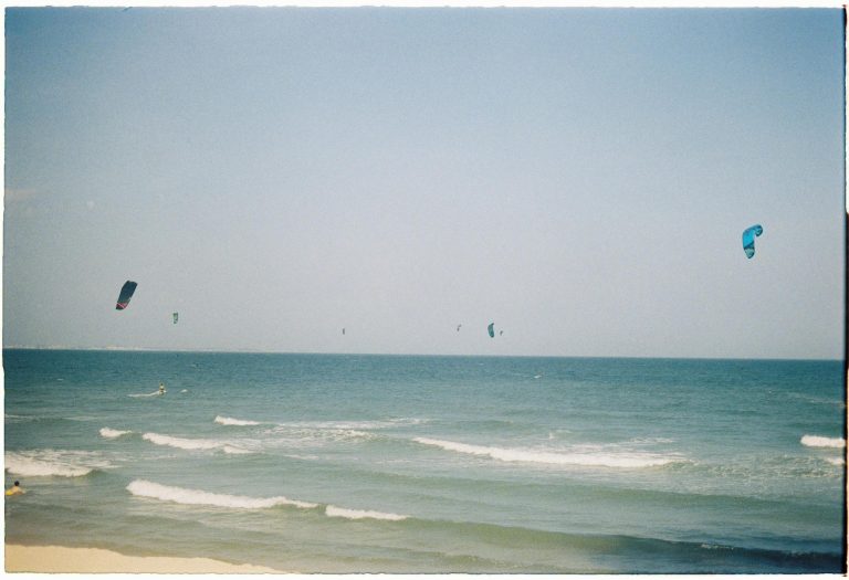 Kitesurfers glide over ocean waves on a sunny day, capturing the thrill of watersports.