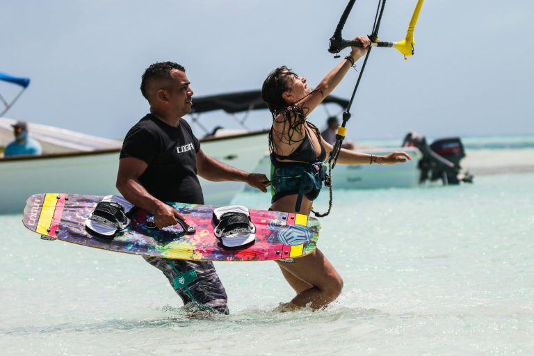 Man assisting woman with kitesurfing on a sunny tropical beach, enjoying the thrill and recreation.