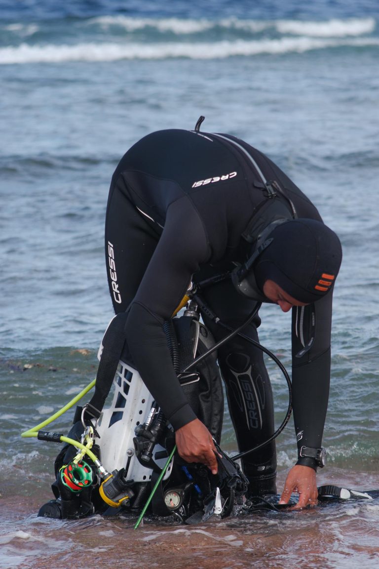 Scuba diver in wetsuit preparing equipment at the beach, ready for an underwater adventure.
